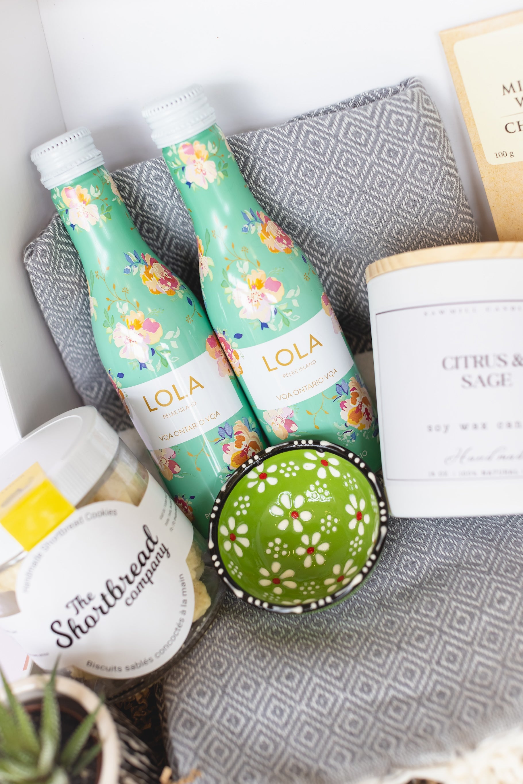 Two floral-patterned bottles labeled 'LOLA' on a textured surface with a candle and cookie jar.